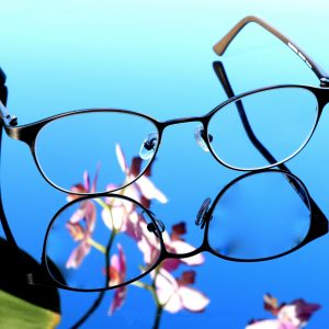 Stylish eyeglasses on reflective surface with orchid blossoms. Perfect for design inspiration.